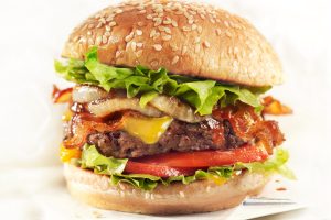 Cận cảnh một chiếc hamburger với đầy đủ thành phần nguyên liệu cơ bản như thịt, salad, cà chua, hành tây và phô mai kẹp trong 2 lát bánh mì mềm thơm